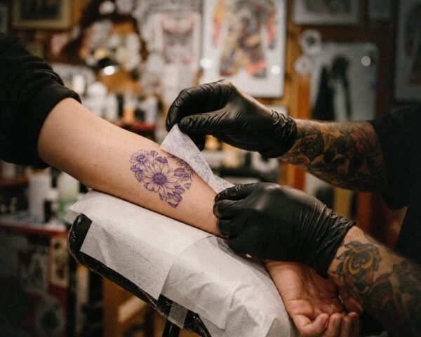 A tattoo artist wipes a fresh flower tattoo on a client's forearm