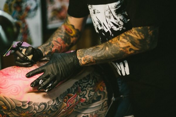 A tattoo artist with tattooed arms works on a colour back piece